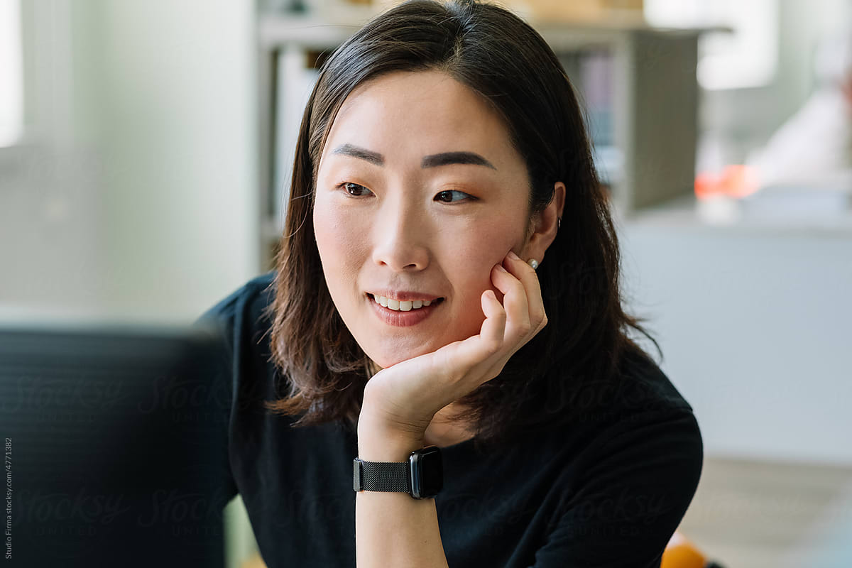 A woman in a black sweater looking thoughtfully at her computer